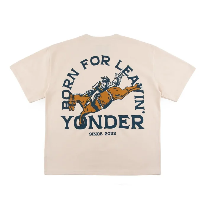 Cream short-sleeve tee, small navy chest print, large arched back graphic of a bronc rider in orange and navy, woven label; detail shots of the print, label and hem